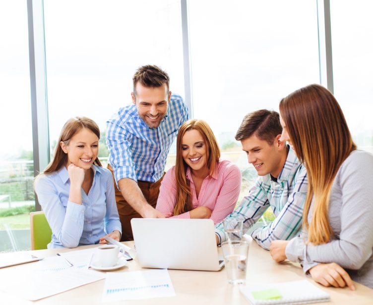 Colleagues gathered around a laptop, smiling
